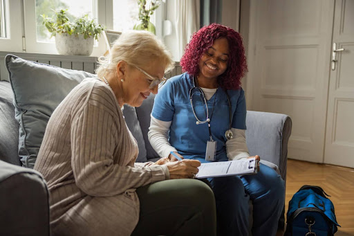 A smiling nurse sits beside a senior woman signing documents, illustrating the reality behind the franchise myth that starting a home health business requires a fortune.