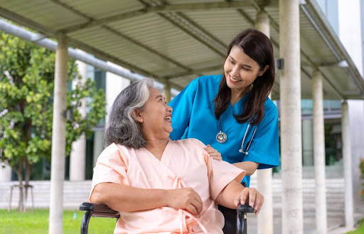A caregiver smiles warmly at a senior woman in a wheelchair outside a care facility, symbolizing the rising gold rush in the home care industry for those who enter the market wisely.