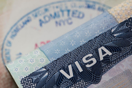A close-up of a U.S. visa with an immigration stamp in the background, representing the pathway for a foreign national to legally own and operate a home care business in the United States.