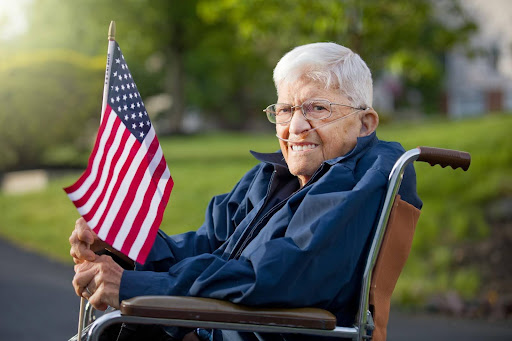 An elderly veteran in a wheelchair proudly holds an American flag, symbolizing the growing demand for home health franchise services across U.S. cities with aging populations.