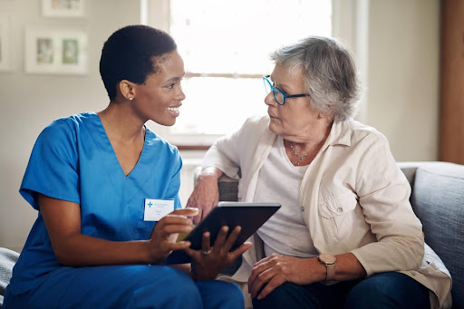 Smiling caregiver showing a senior woman information on a tablet—highlighting the profit potential of running a home care franchise compared to other businesses like daycare.