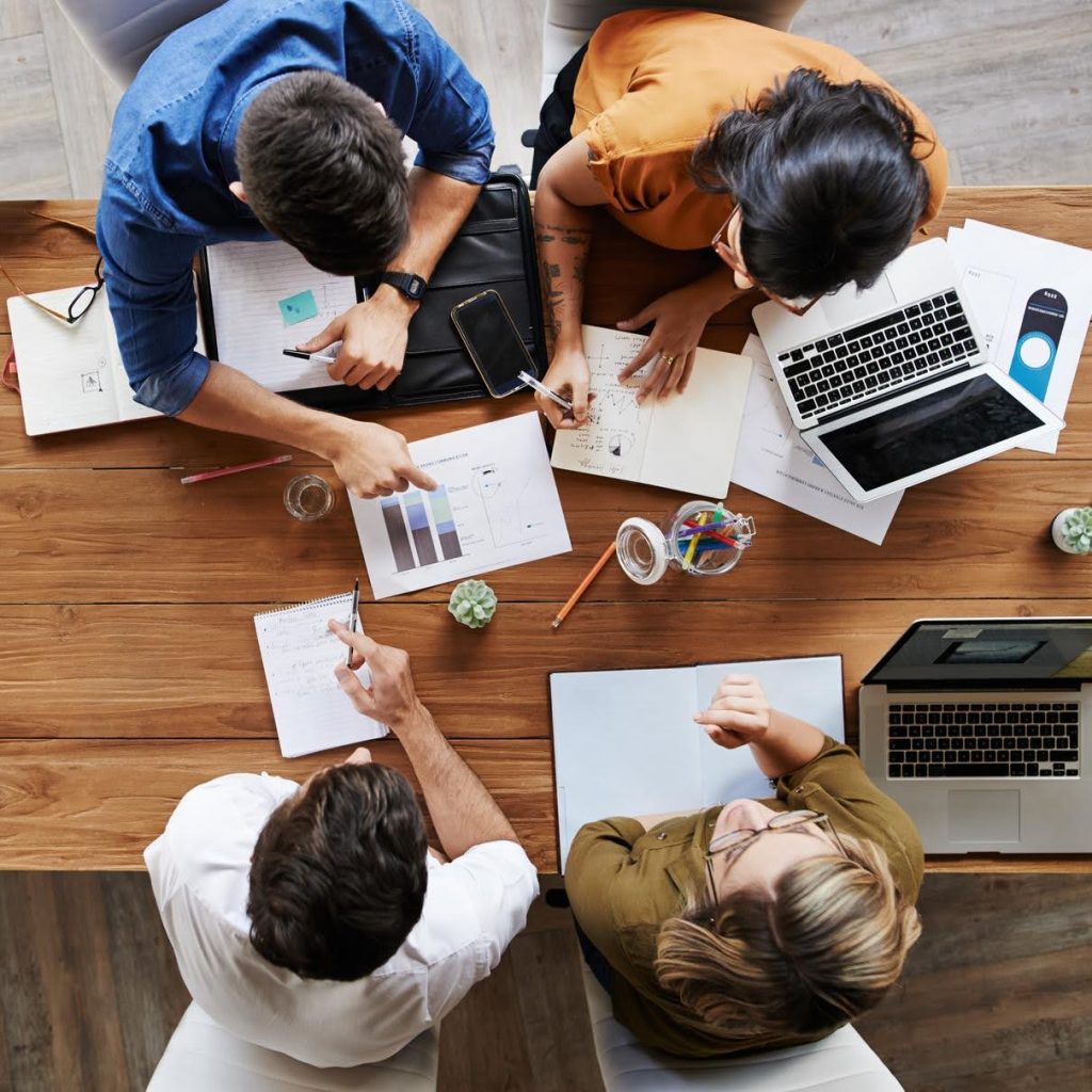 Group of professionals collaborating over charts and laptops at a table, discussing ways to grow revenue in a non-medical home care business.