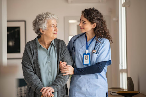Caregiver in scrubs offering support to an elderly woman at home, highlighting the irreplaceable human touch in care—even in the age of AI advancements.