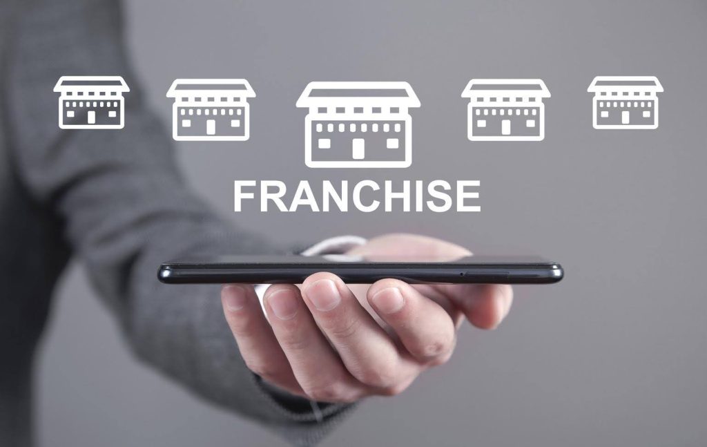 Hand holding a smartphone with icons of franchise locations above it, symbolizing a good home care franchise model.