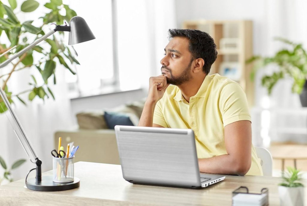 Man sitting thoughtfully at a desk with a laptop, symbolizing whether strong English skills are necessary to successfully run a franchise.