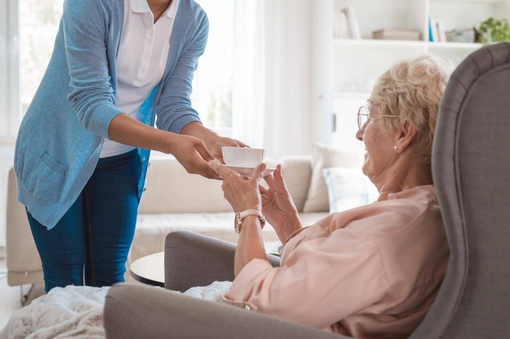 Caregiver offering tea to an elderly woman at home, symbolizing how home care provides a recession-resilient franchise model by meeting essential needs.