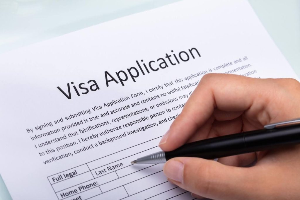 Hand filling out a visa application form, symbolizing the steps to qualify for the E-2 visa through a home care franchise opportunity.