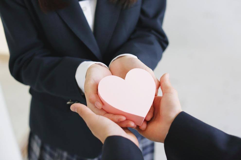 Close-up of a person handing a pink heart-shaped object to another, symbolizing empathy, compassion, and care as essential qualities in successful franchise ownership.