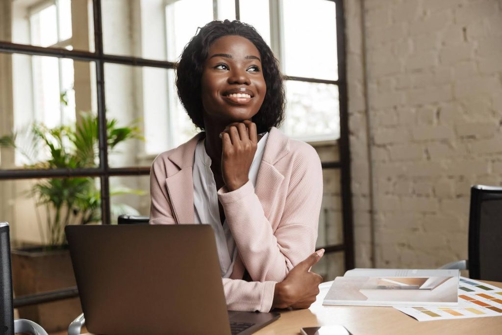 Smiling foreign entrepreneur sitting at a desk with a laptop, representing opportunities to start a U.S. business through the E2 Visa program.