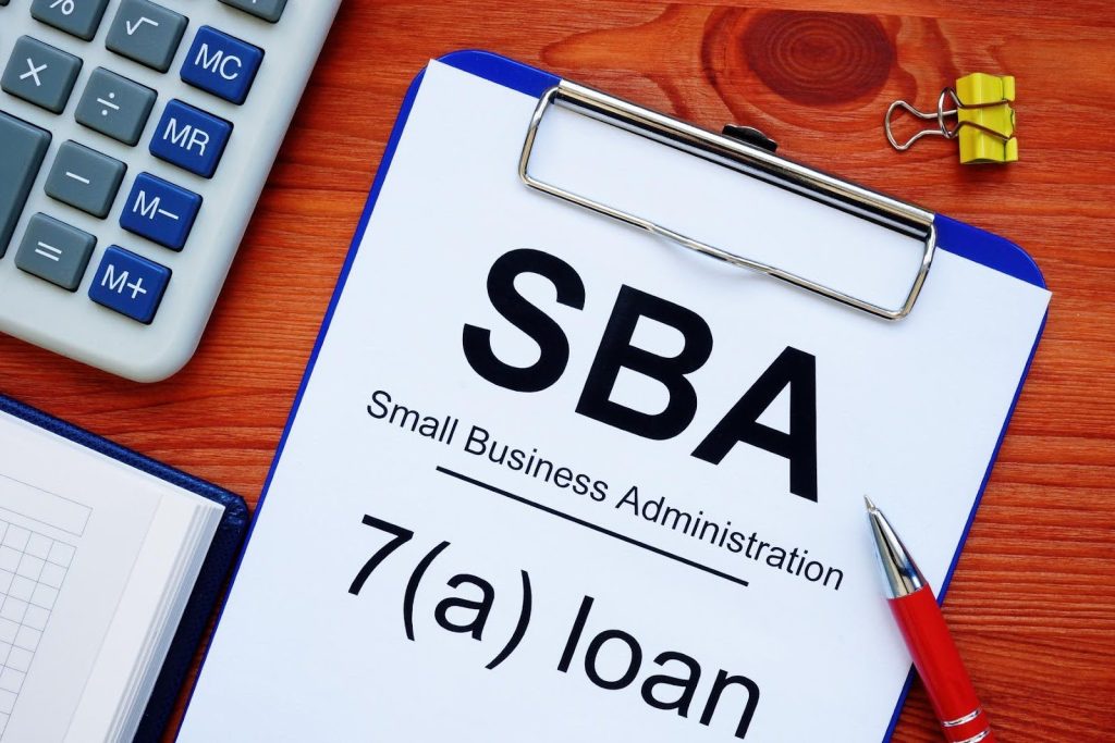 Clipboard showing SBA 7(a) loan paperwork beside a calculator and pen, representing the realities of SBA franchise loans.