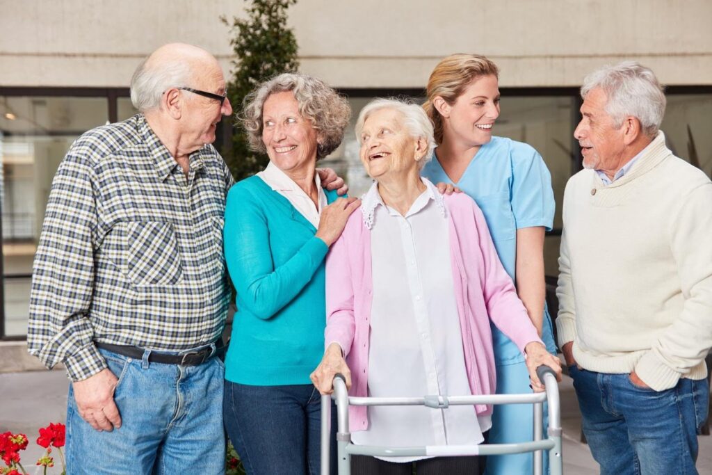 Group of smiling seniors talking with a caregiver outdoors, representing the growing aging population and the future demand for senior care franchises by 2030.