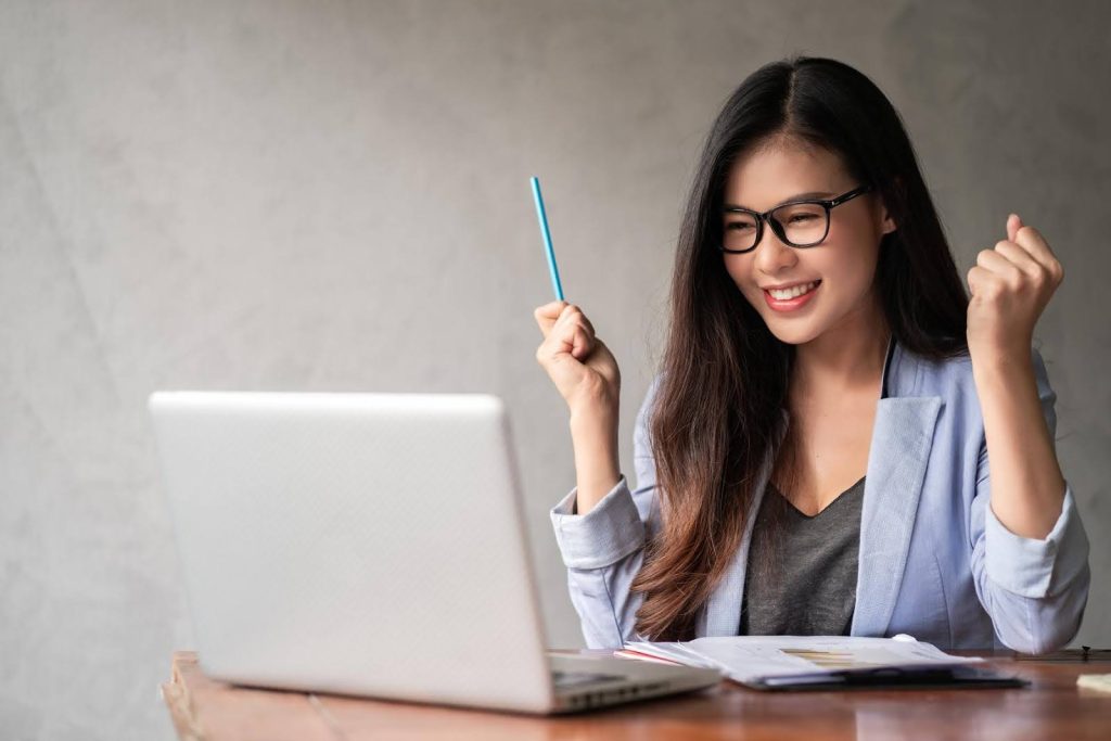Woman celebrating while working on a laptop, representing how entrepreneurs can run a home care franchise from another state.