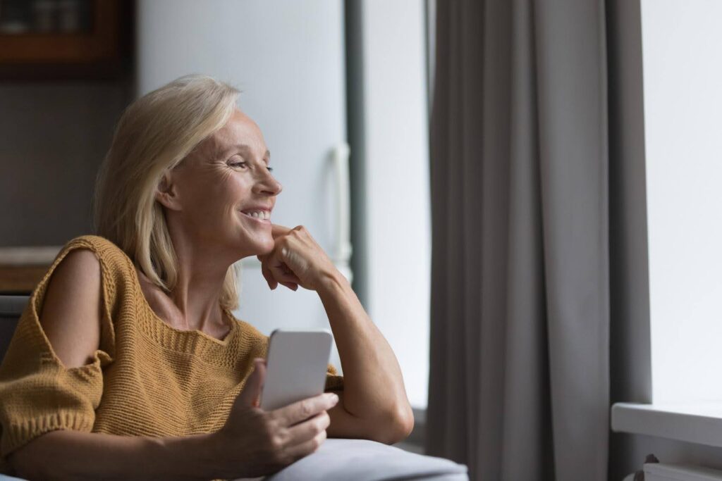 Confident woman in her 50s using a smartphone at home, representing how people can successfully start an Ace Home Care Franchise later in life and build a meaningful business