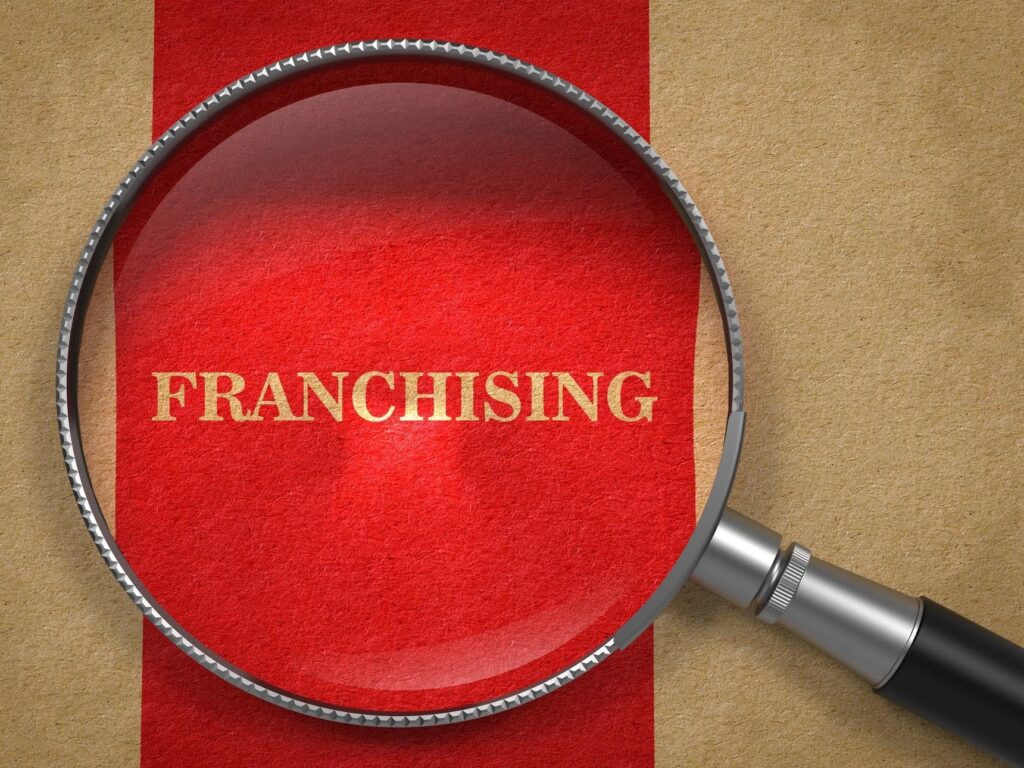 Magnifying glass highlighting the word "Franchising," representing how Ace Home Care Franchise helps reduce risk through proven systems, training, and ongoing support