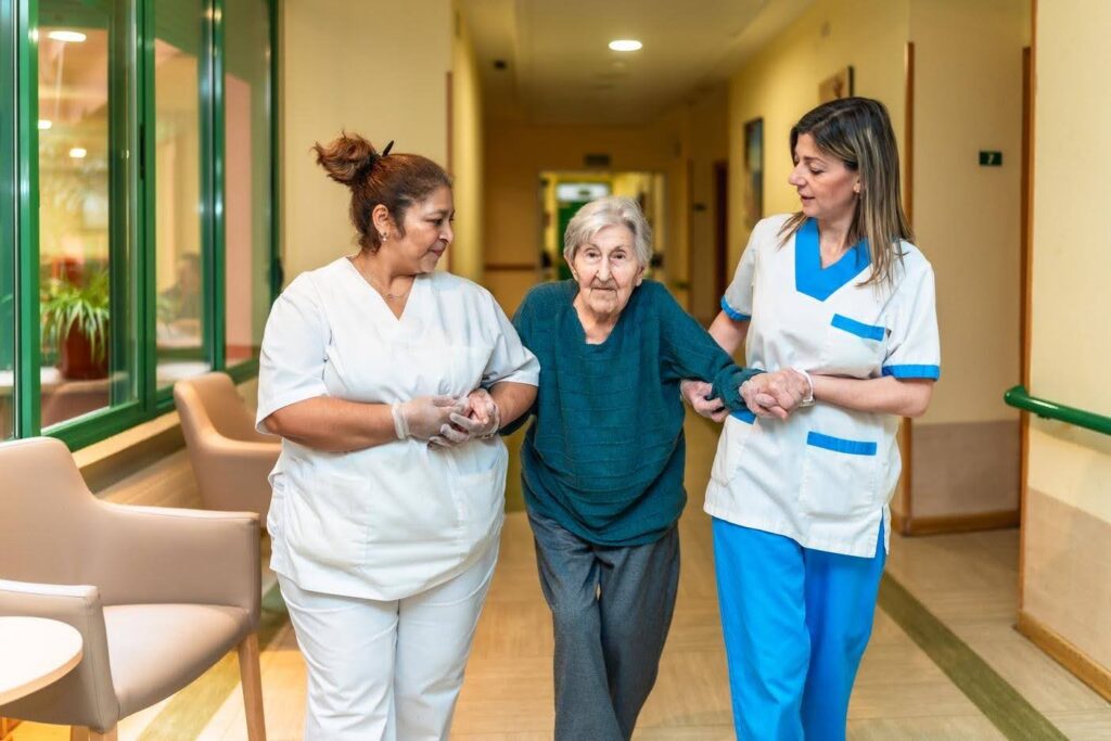 Retired nurse supporting an elderly woman with a caregiving team, highlighting how Ace Home Care Franchise helps retired healthcare professionals start a rewarding home care business.